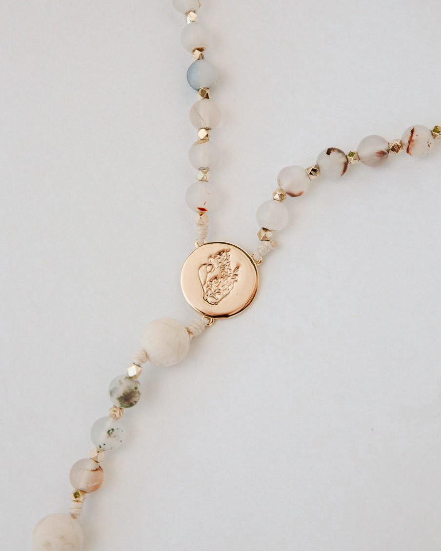 Rosary with beige beads and a gold pendant on a light gray background
