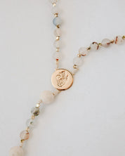 Rosary with beige beads and a gold pendant on a light gray background