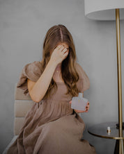 Woman in a brown dress holding holy water bottle against a neutral background