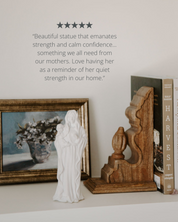Statue of a woman holding a child on a shelf with decorative items and a book.
