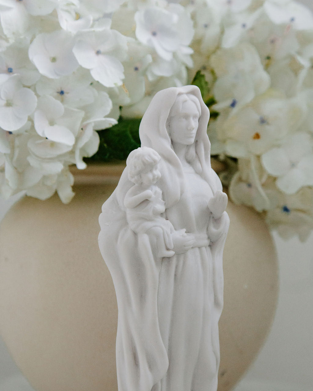 White statue of a woman holding a child in front of white flowers