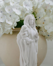 White statue of a woman holding a child in front of white flowers