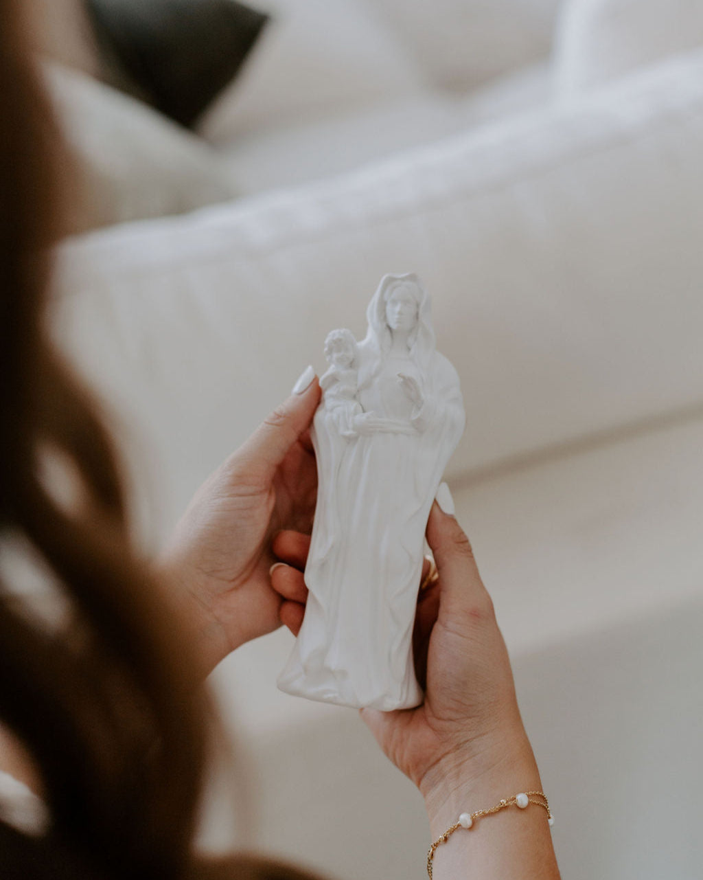 Person holding a white statue of a woman with a child against a blurred background