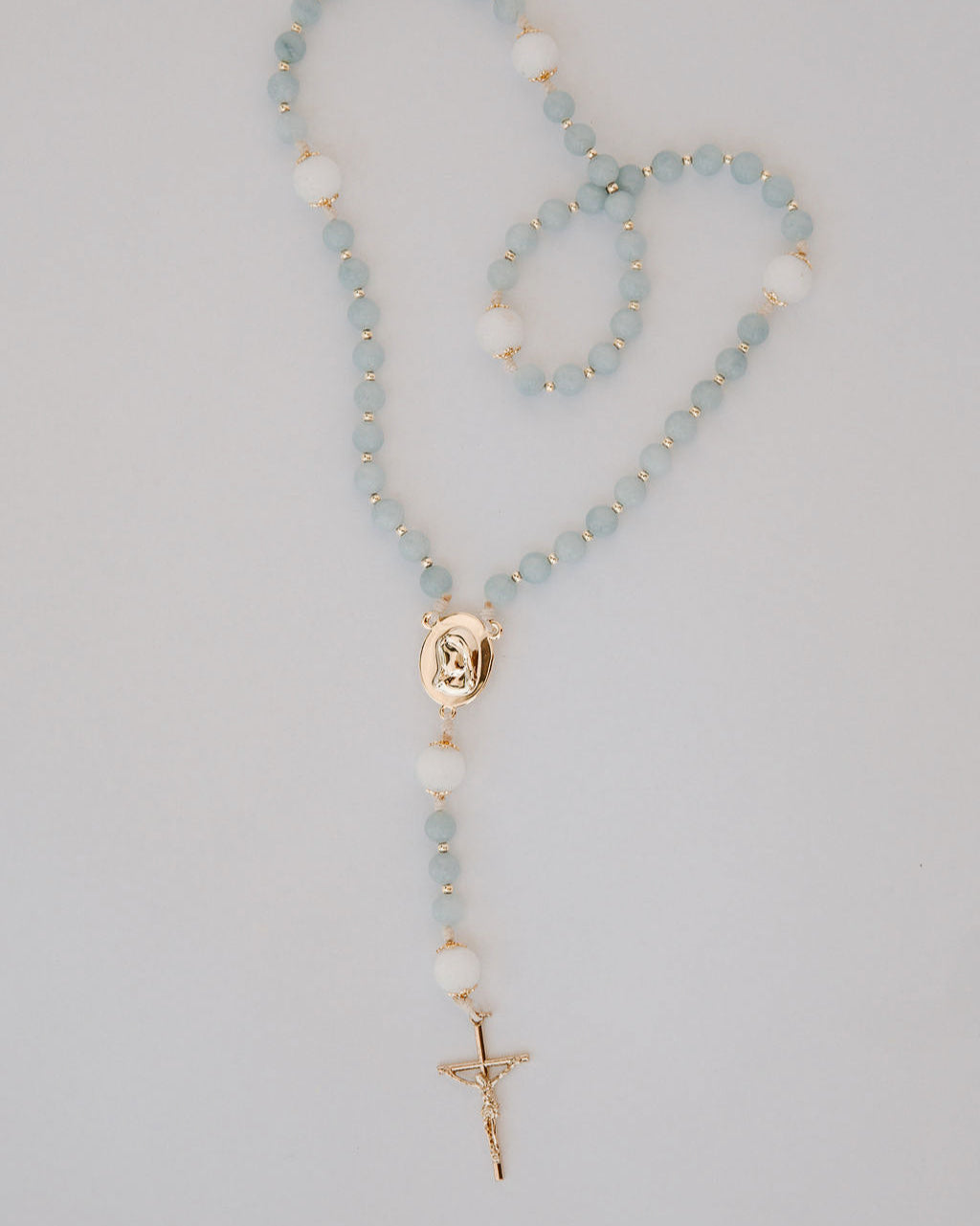 Rosary with light blue beads and gold accents on a gray background