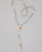 Rosary with light blue beads and gold accents on a gray background