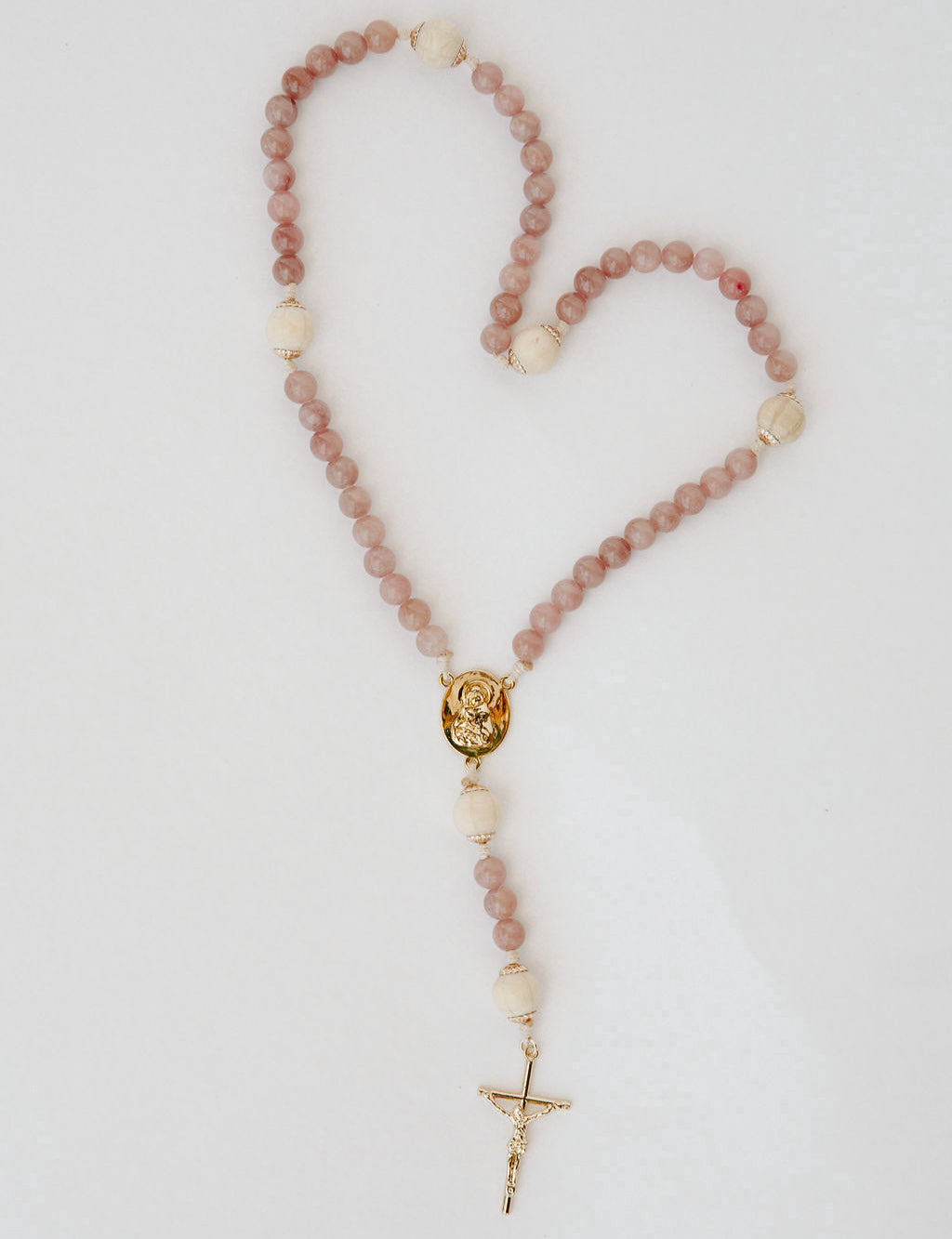Rosary with pink and wood beads and a gold cross on a light gray background