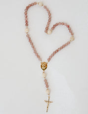 Rosary with pink and wood beads and a gold cross on a light gray background