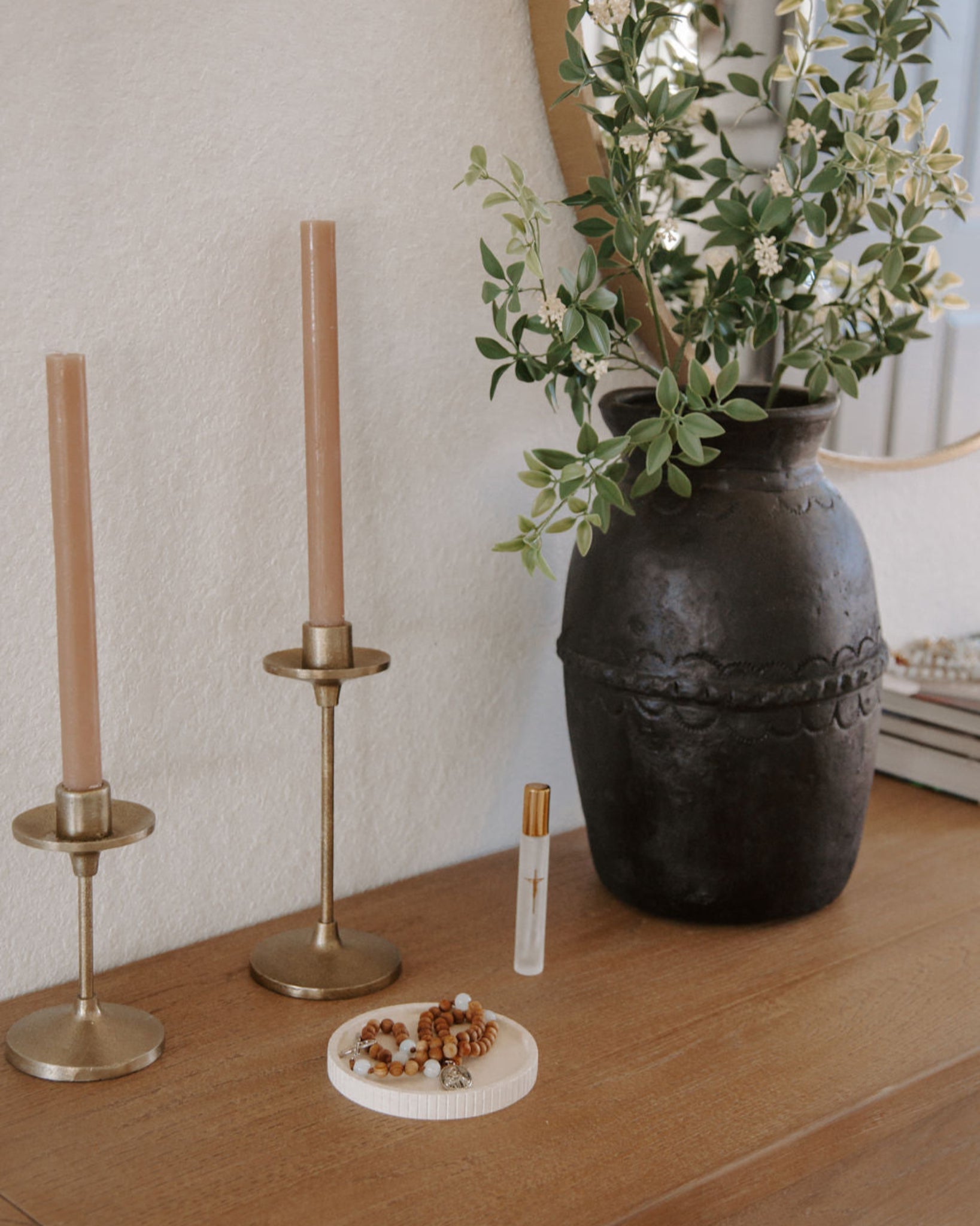 Decorative items including a rosary dish, vase with flowers, candles, and holy water spritzer on a wooden surface.