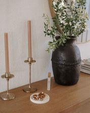 Decorative items including a rosary dish, vase with flowers, candles, and holy water spritzer on a wooden surface.