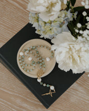 Rosary dish with gemstone rosary surrounded by white flowers on a wooden surface.