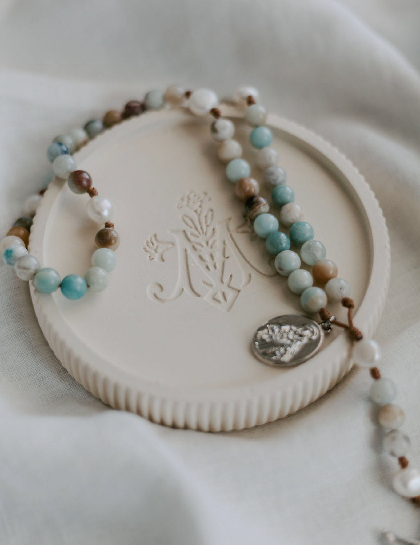 Rosary dish with gemstone rosary on fabric background