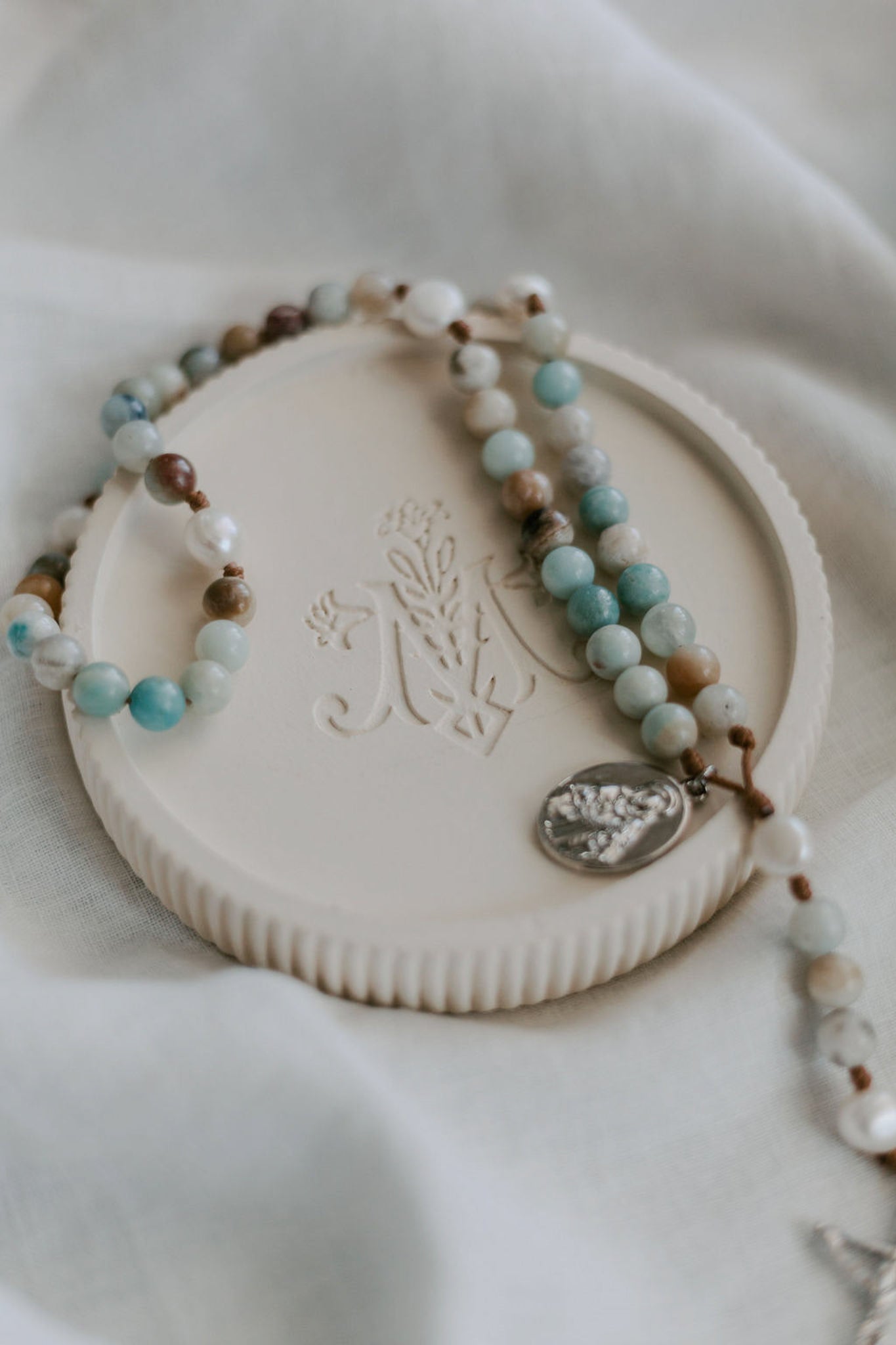 Rosary dish with gemstone rosary on fabric background