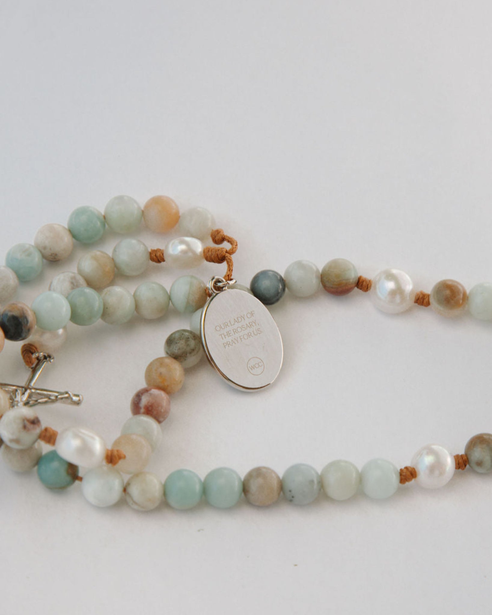 Multicolored beaded rosary with a silver medal on a light gray background