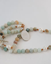 Multicolored beaded rosary with a silver medal on a light gray background