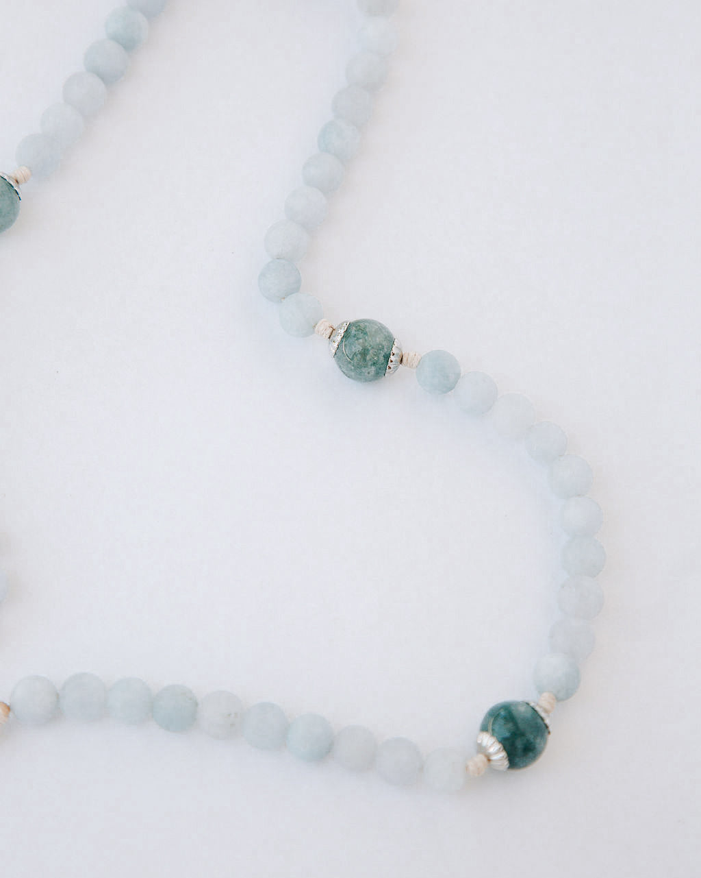Rosary with alternating light blue and green beads on a white background