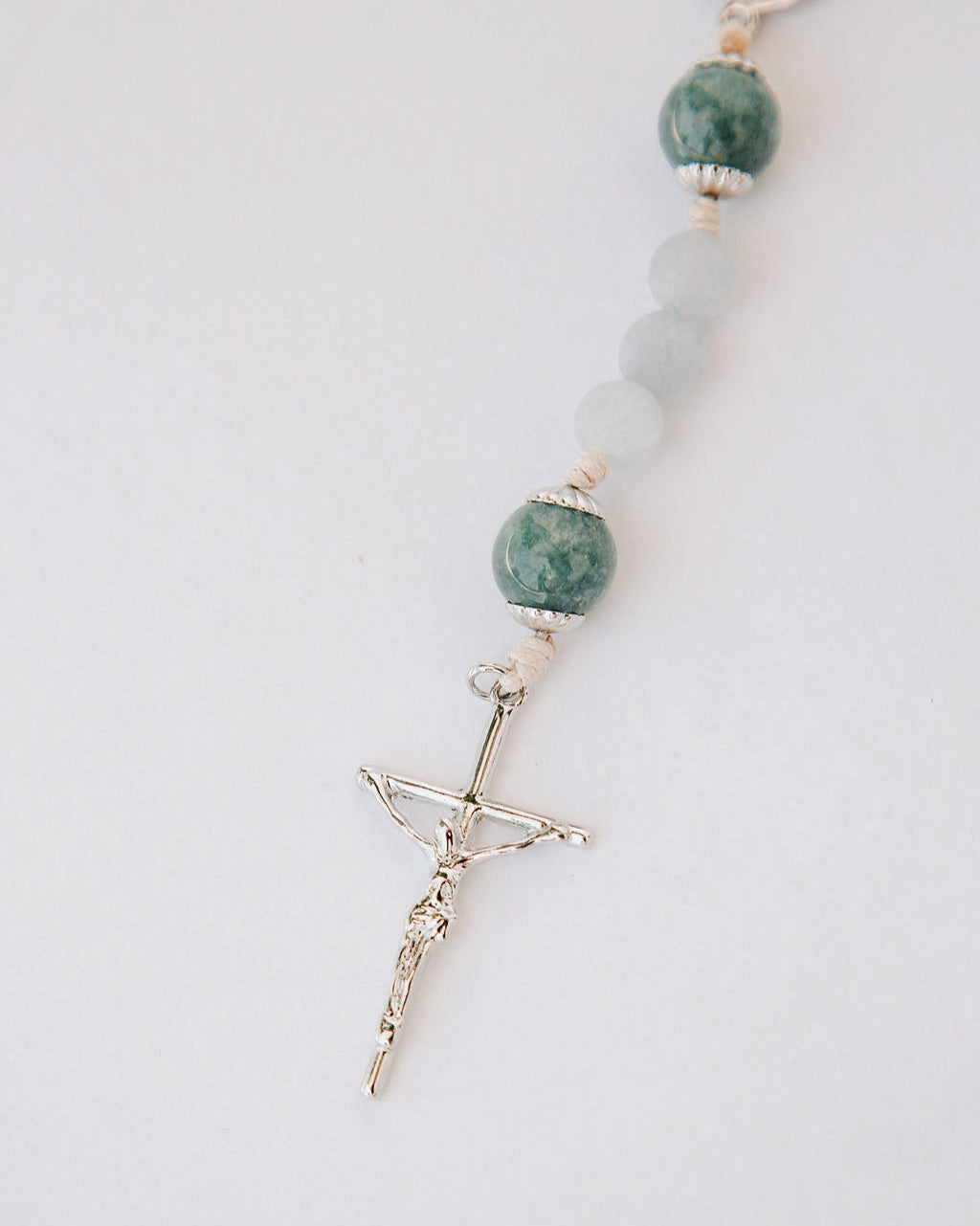 Rosary with pale blue beads and a silver cross on a light gray background
