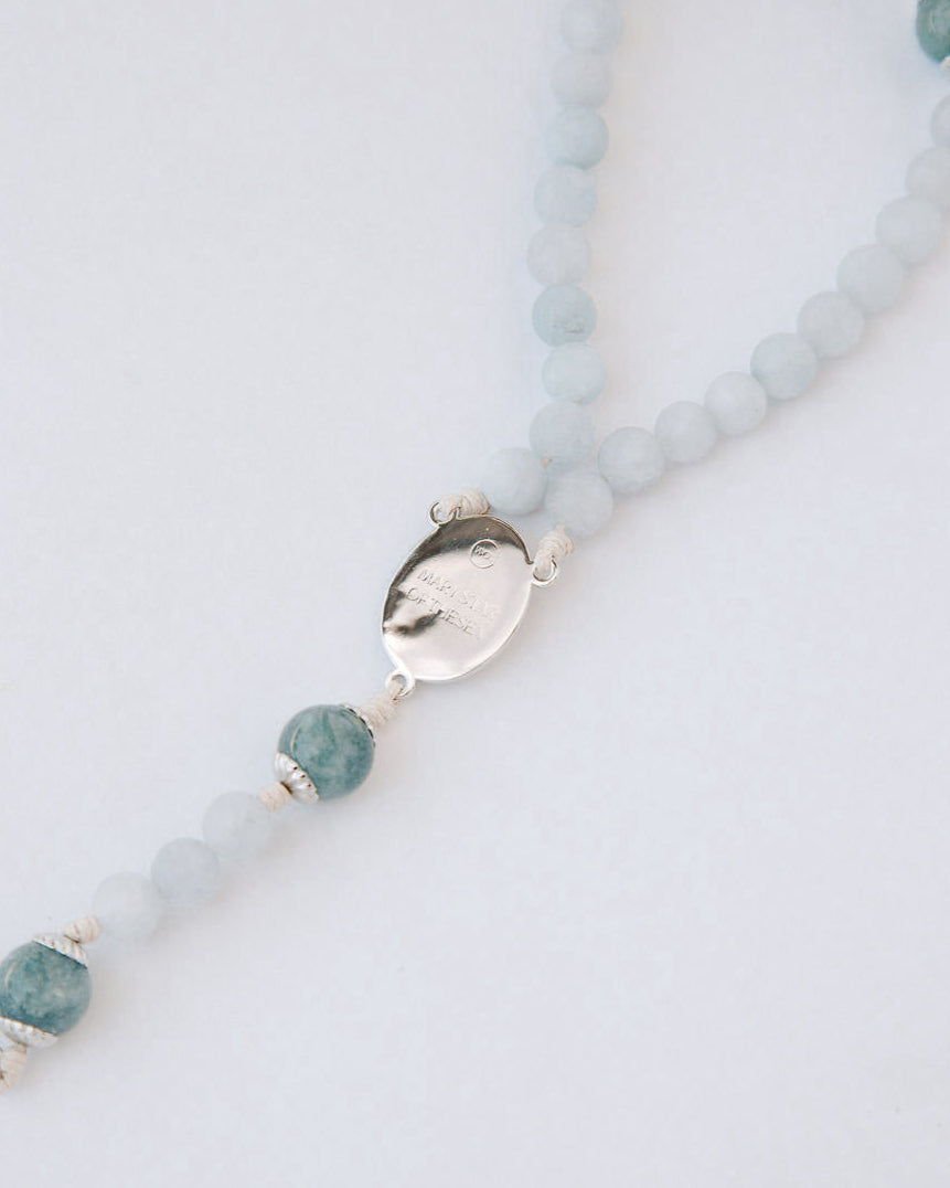 Rosary with blue beads and silver medal on a light gray background