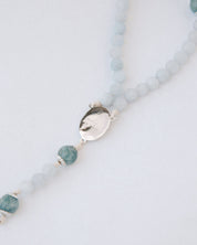 Rosary with blue beads and silver medal on a light gray background