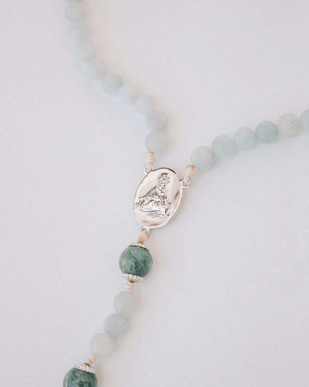 Rosary with blue beads and a silver medal on a light gray background