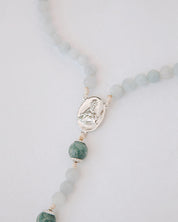 Rosary with blue beads and a silver medal on a light gray background