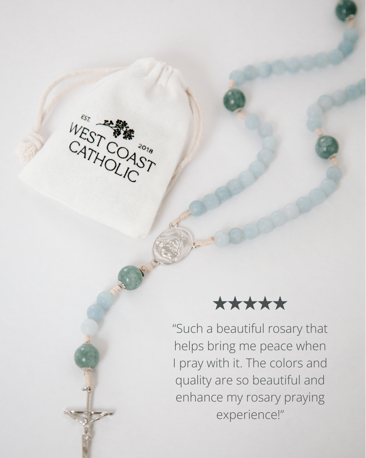 Rosary with blue beads and a silver cross on a white background, accompanied by a drawstring bag labeled 'West Coast Catholic'.