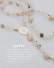 Rosary with beige beads and a gold charm on a light gray background