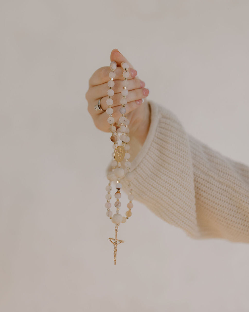 Woman's hand holding rosary with multicolor pink beads