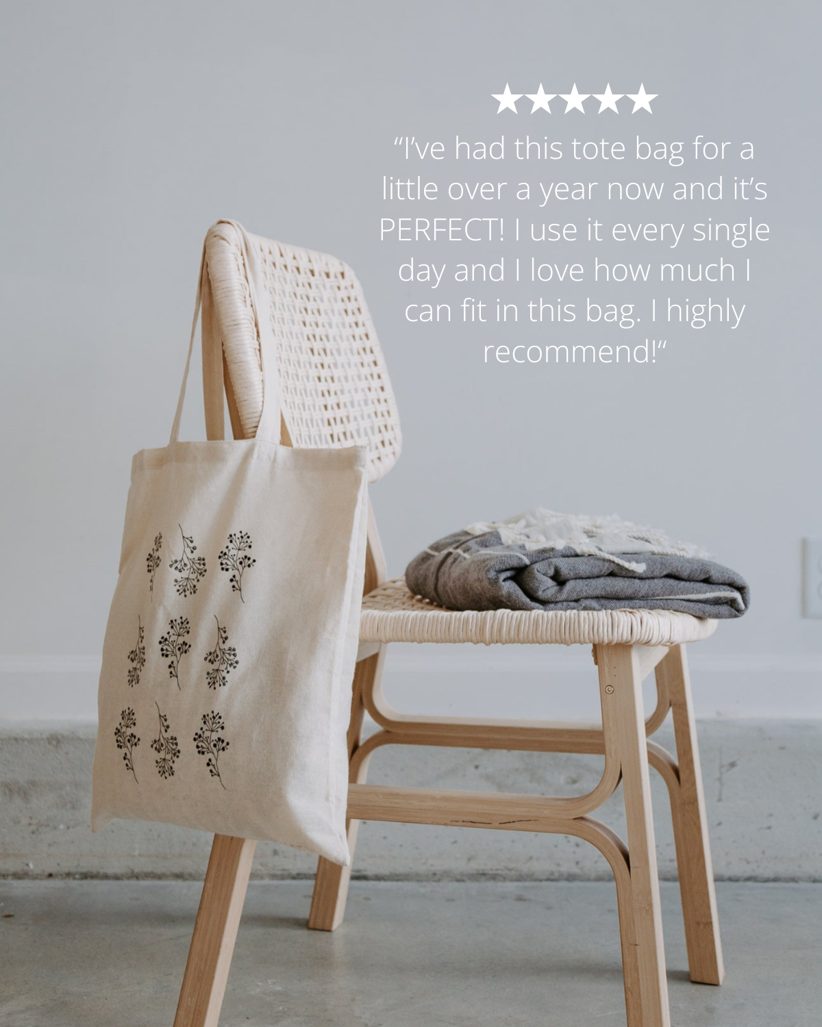 Beige tote bag with floral patterns hanging on a wooden chair against a light gray wall.