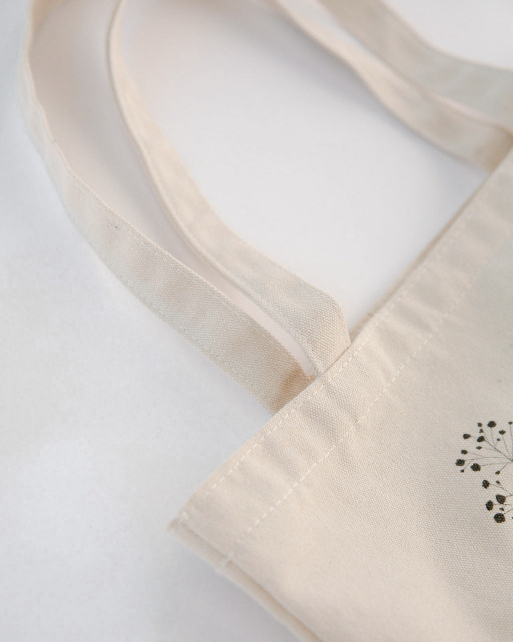 Close-up of a beige tote bag with a small black design on a light gray background