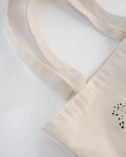 Close-up of a beige tote bag with a small black design on a light gray background