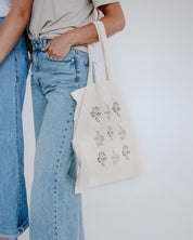 Person holding a tote bag with floral designs on a plain background