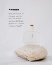 Holy water bottle with a rock on a light gray background, featuring a five-star rating and customer review.