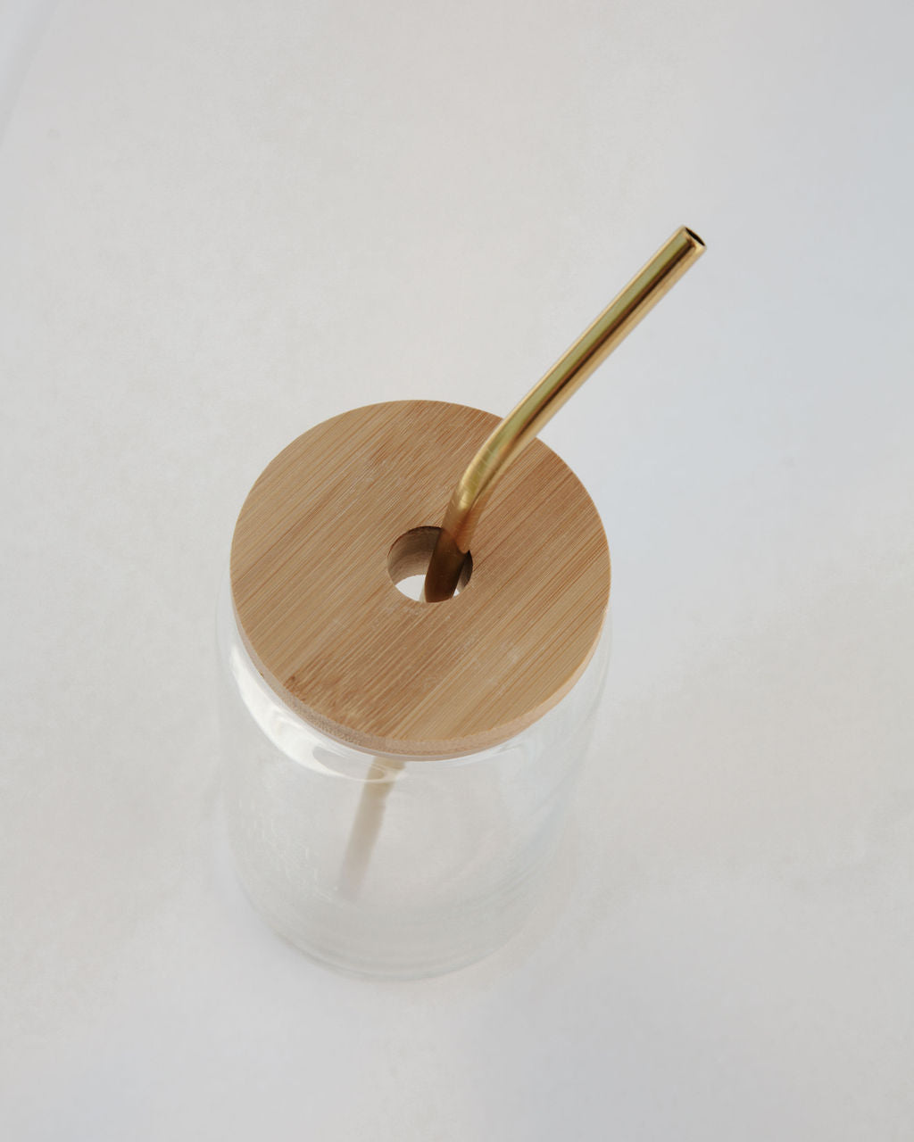 Clear glass drink container with a bamboo lid and straw on a white background