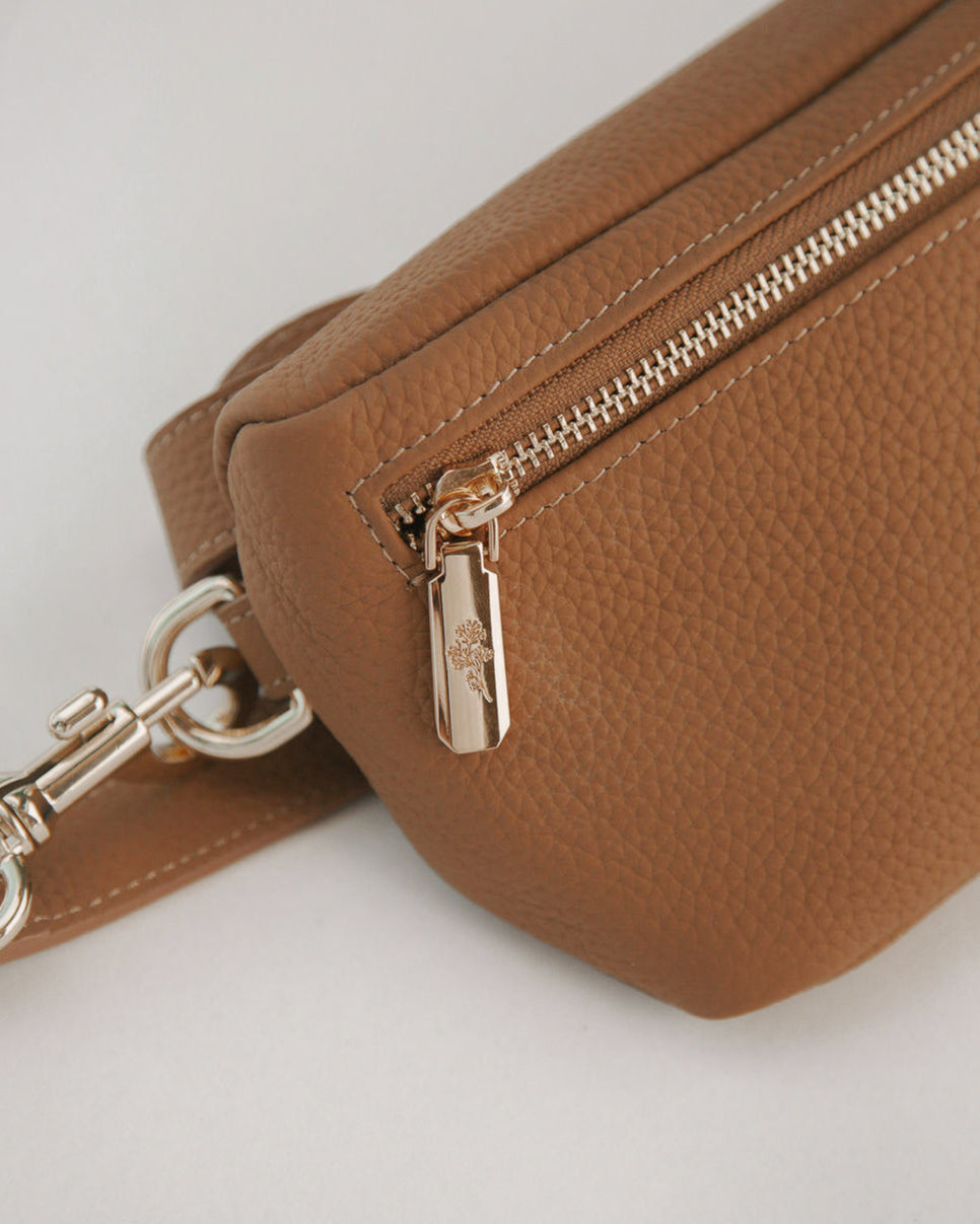 Brown leather bag with gold zipper and clasp on a light gray background
