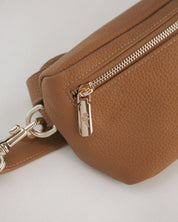 Brown leather bag with gold zipper and clasp on a light gray background
