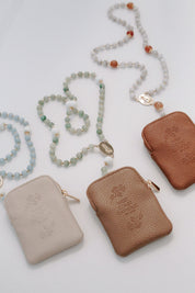 Three leather pouches in beige, brown, and brown with rosaries on a light gray background