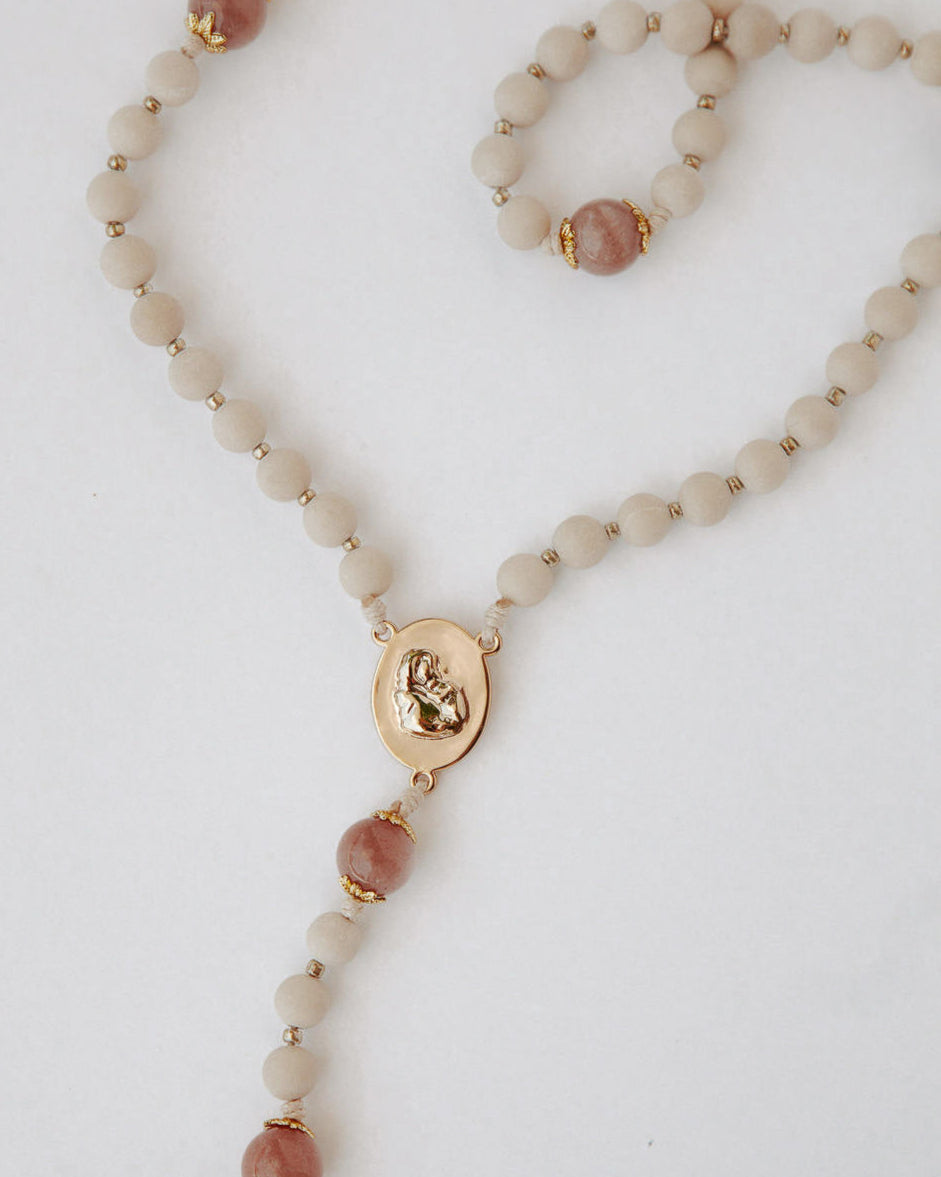Rosary with beige and pink beads and gold accents on a white background