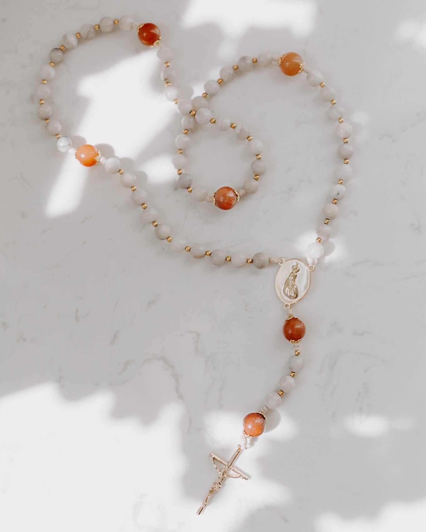 Gemstone rosary with orange and neutral beads on a marble background