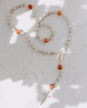 Gemstone rosary with orange and neutral beads on a marble background