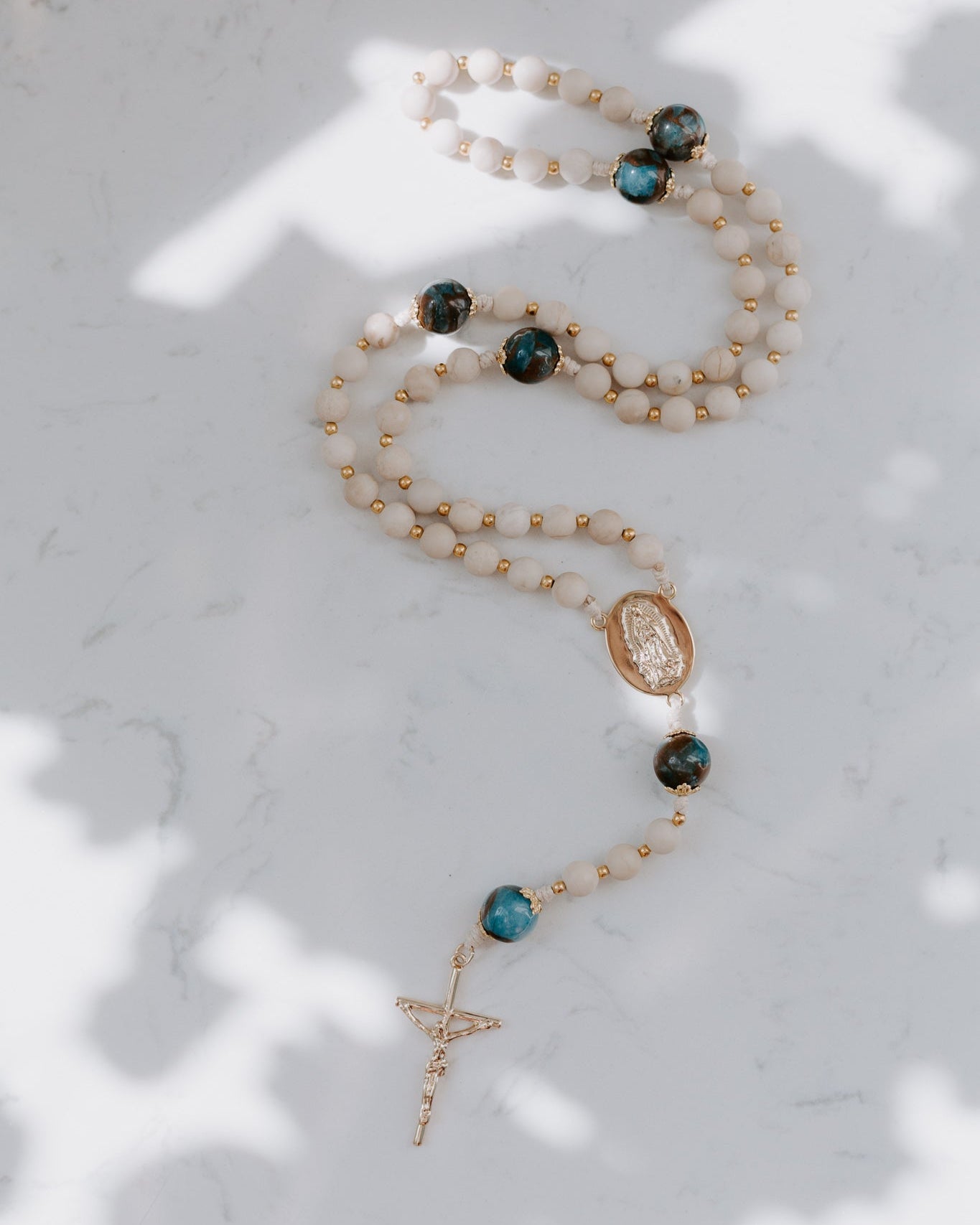 Rosary with teal and tan beads on a marble background