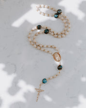 Rosary with teal and tan beads on a marble background