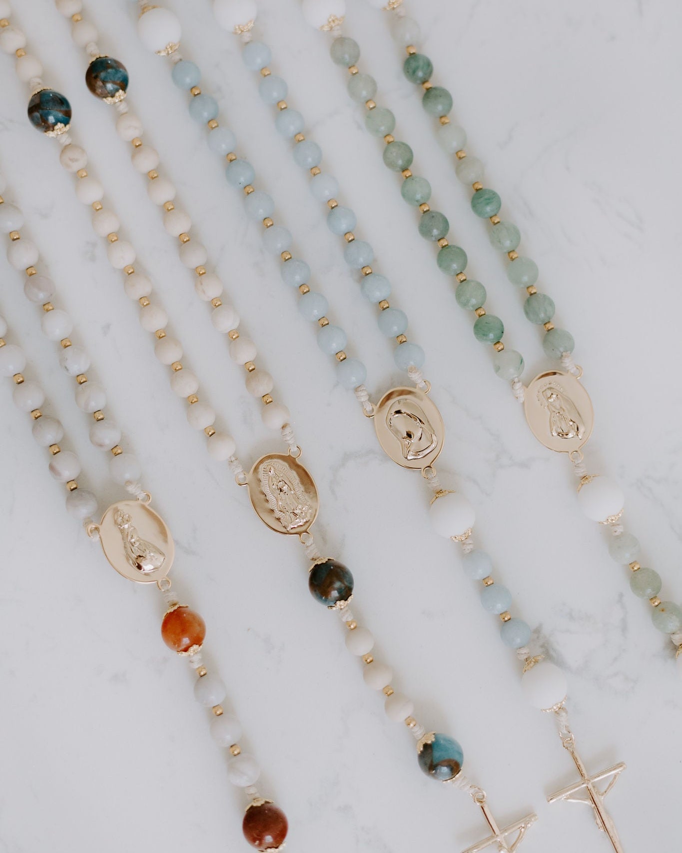 Beaded rosaries with gold medals on a marble surface