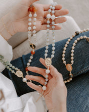 Hands holding multiple beaded rosaries with various stones and pendants.