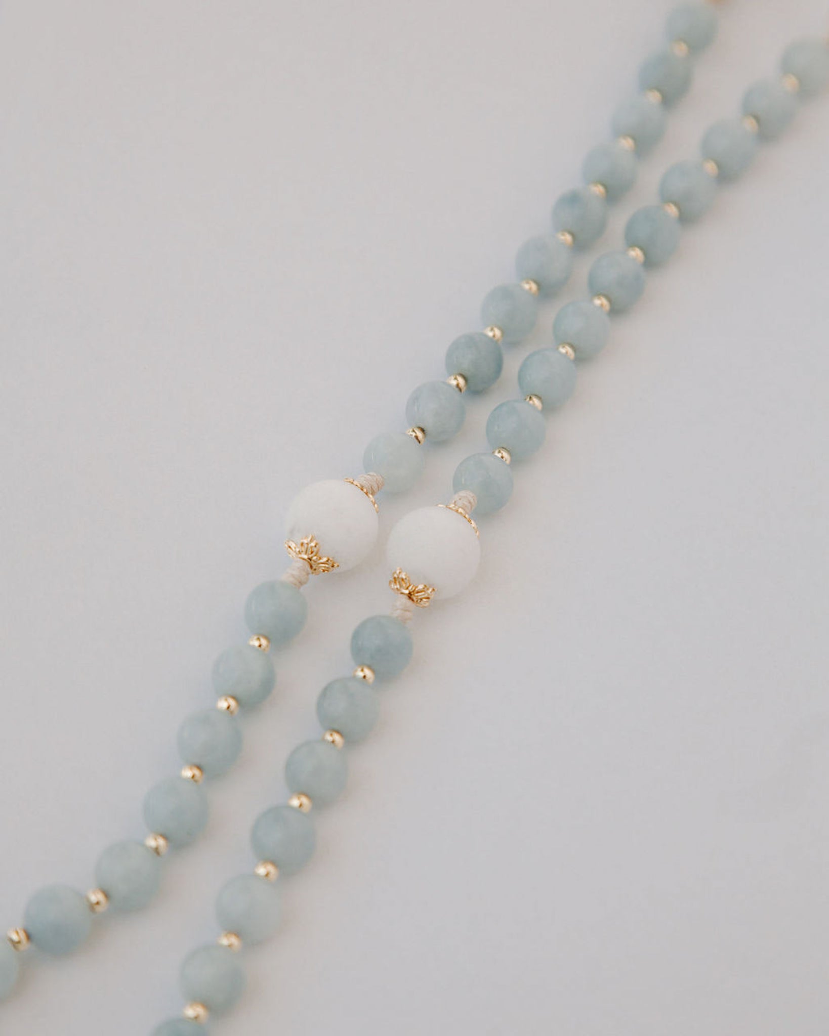 Beaded rosary with light blue beads and gold accents on a white background