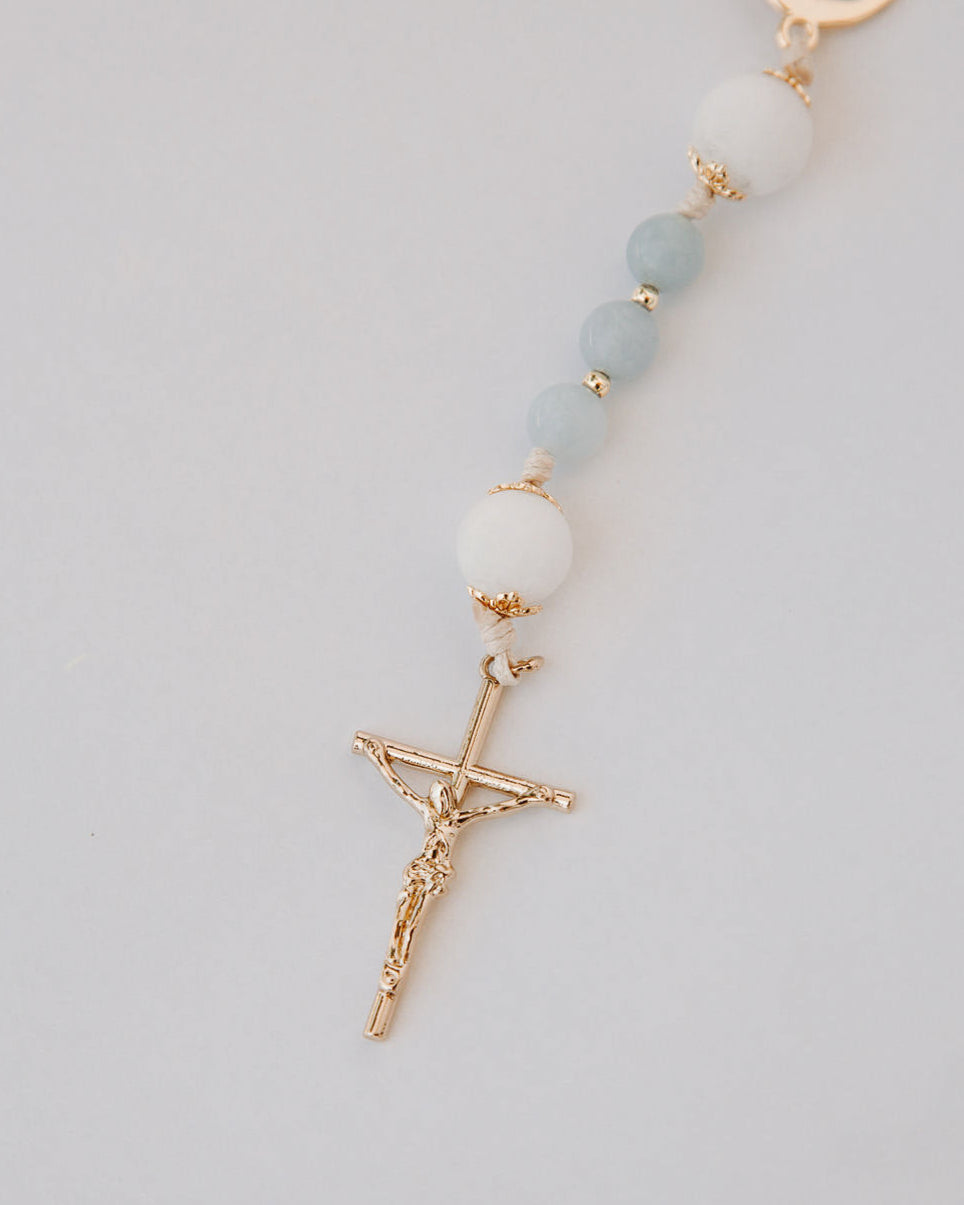 Gold medal rosary with light blue and white beads on a light gray background