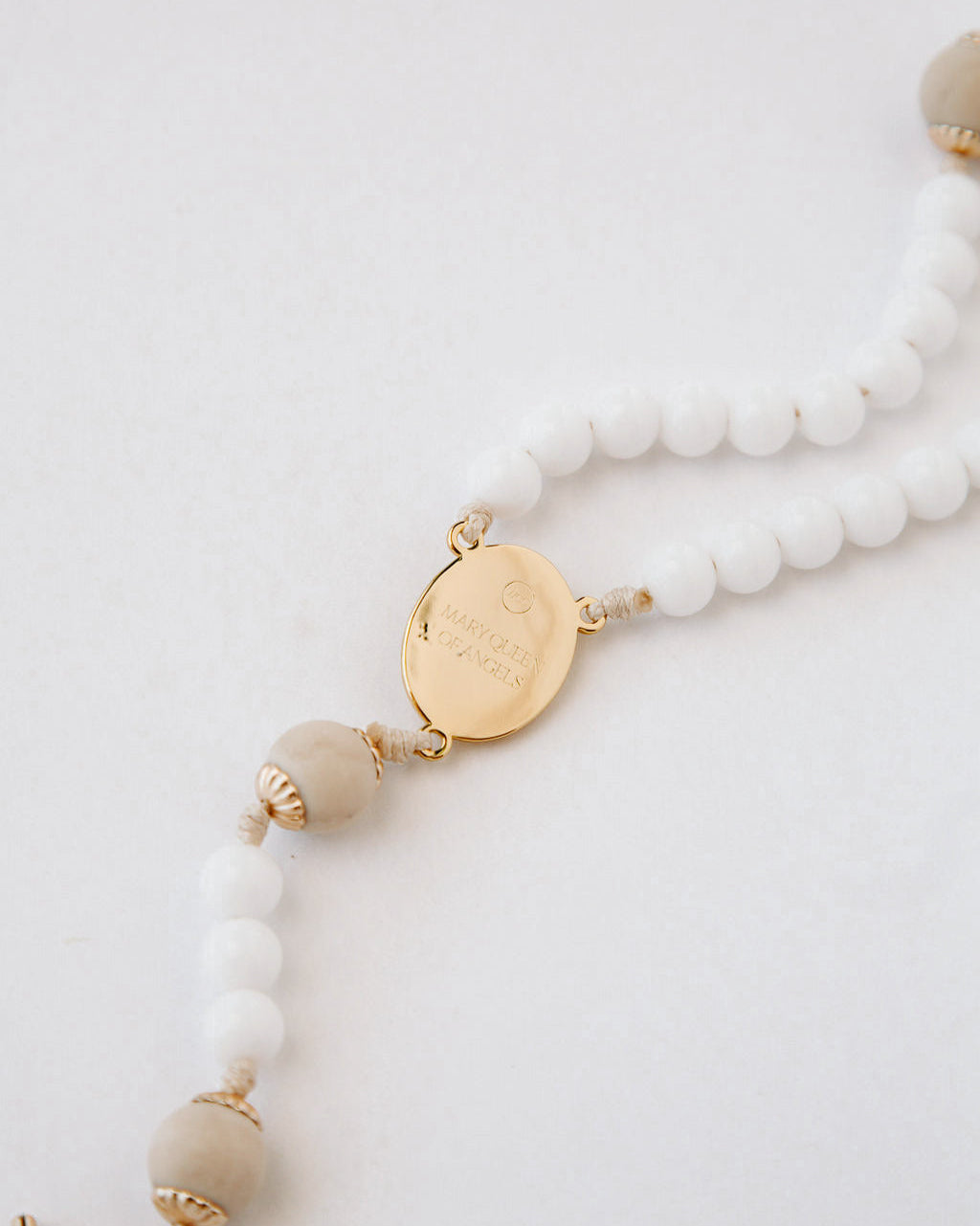 Rosary with white beads and gold accents on a light gray background