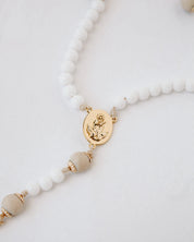 Rosary with white beads and gold accents on a light gray background
