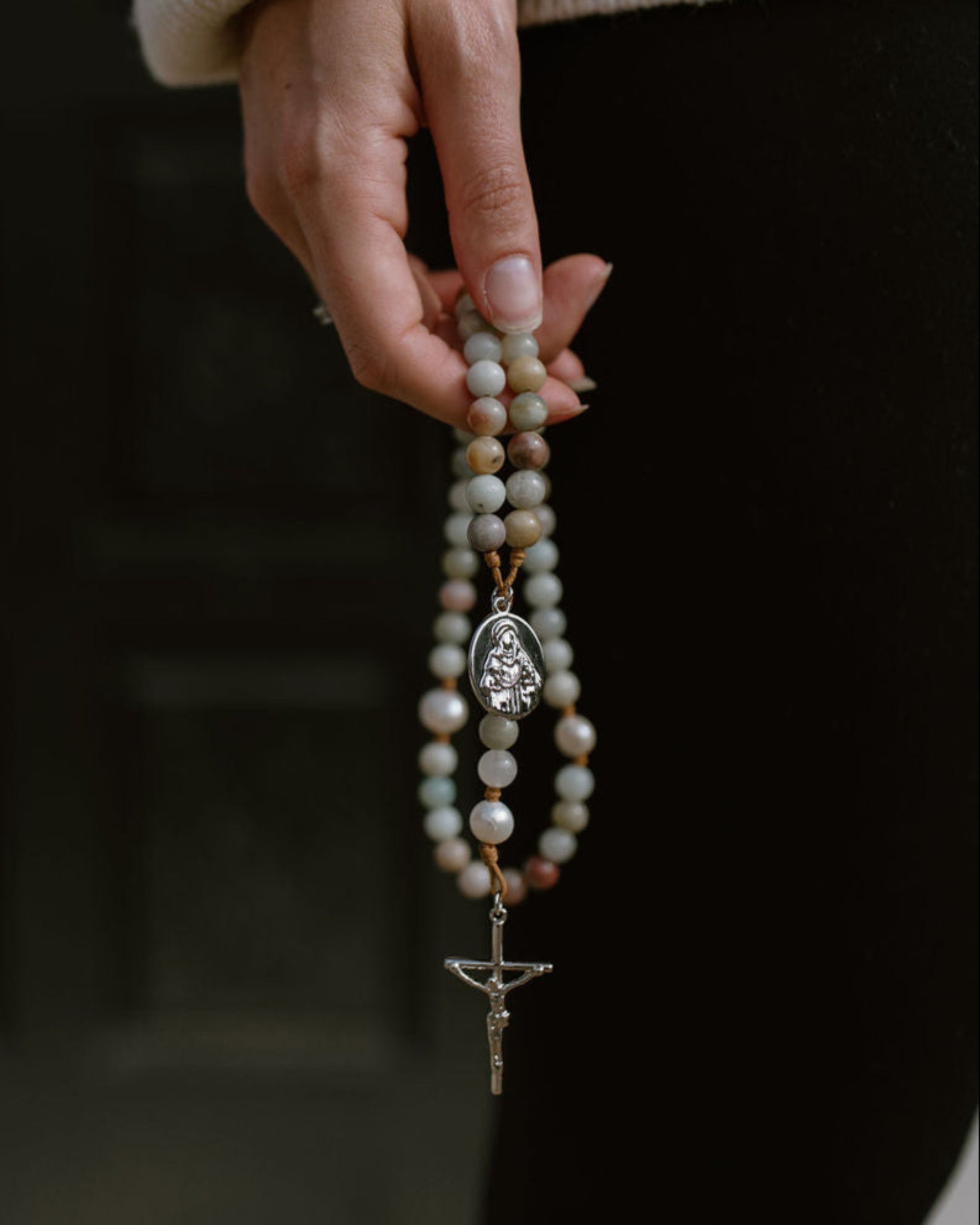 Hand holding a rosary with a blurred background