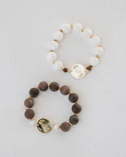 Two rosaries one with white beads and gold accents, and the other with brown beads and gold accents, on a light gray background.