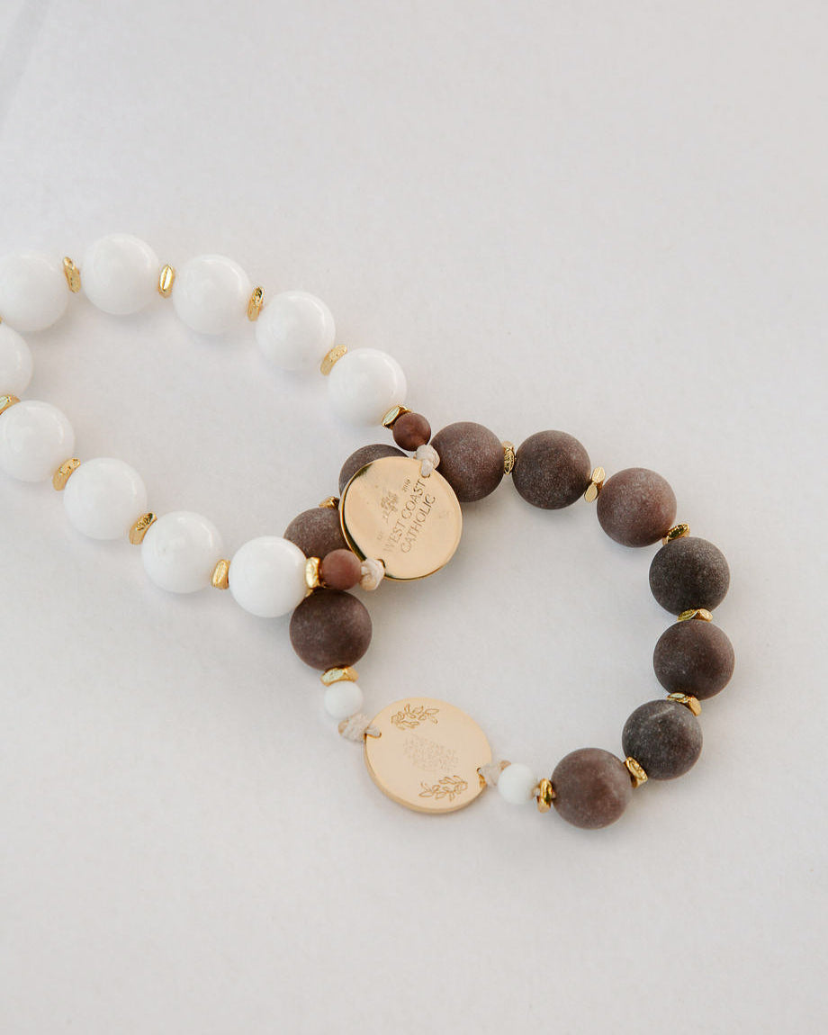 Two beaded rosaries with gold charms on a light gray background